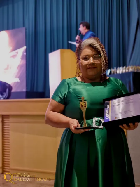 Sol Lima exibe o troféu e a placa em frente ao palco do evento.