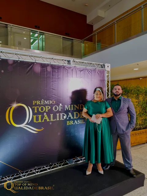 Sol Lima e um acompanhante posam diante do painel Top of Mind Qualidade Brasil.