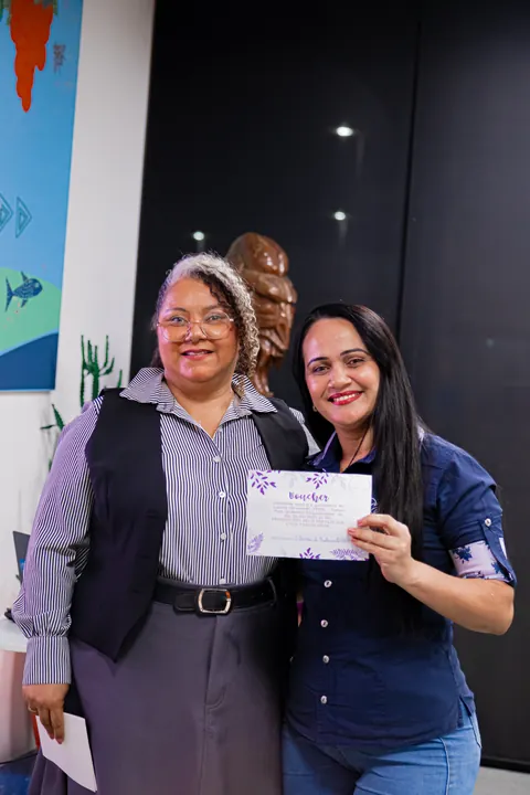 Duas mulheres sorriem juntas segurando materiais do TPMe.